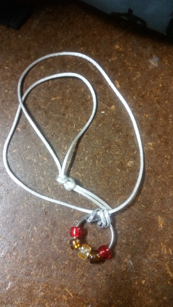 Image Description: a white cord with three chrome-coloured loops, within those three loops is a small metal loop one might use to store keys on, on the loop are five beads with the colour scheme of red-brown-amber-brown-red
