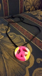 Image Description: There's a necklace with a black cord and a pink-yellow peace symbol